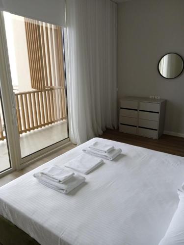 a bedroom with a bed with white sheets and a window at Whisky Green Coast Hotel & Apartments in Palasë