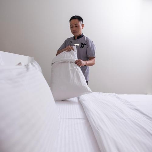 a man standing next to two white beds at Riggae Tower Hotel in Kuwait