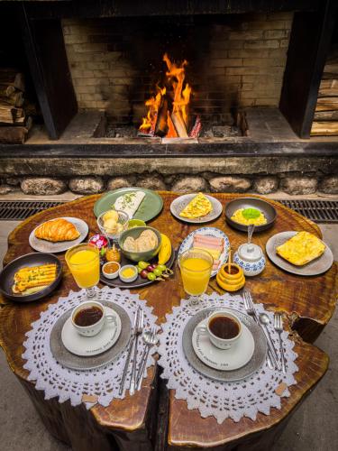 ein Tisch mit Tellern voller Essen und Getränke und ein Kamin in der Unterkunft Hotel Giardino Di Pietra in Gramado