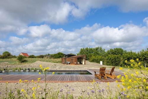 ヴェストカペレにあるHello Zeeland - Tiny House Zeeuwse Liefde 16の池と椅子2脚のある丘の上の家
