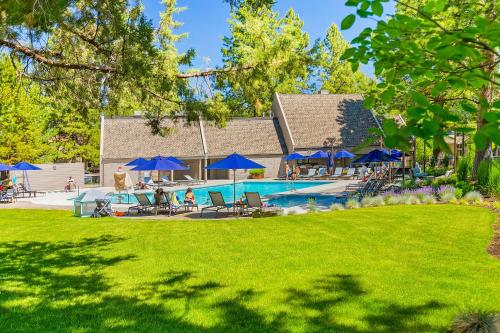 a pool with blue umbrellas and people in a yard at Alpine Studio at Mount Bachelor Village Resort with Pool and Hot Tub in Bend