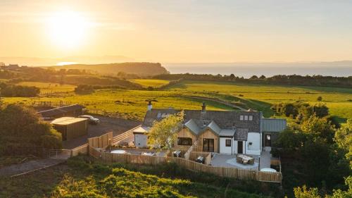 una casa en un campo con el sol en el cielo en Firth View 1 - Luxury Cottage with Sea View & Hot Tub, Ayr, en Ayr