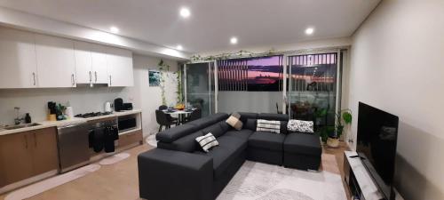 a living room with a black couch and a kitchen at Stylish 1Bedroom Apartment with Study and Parking Near Sydney Airport in Sydney