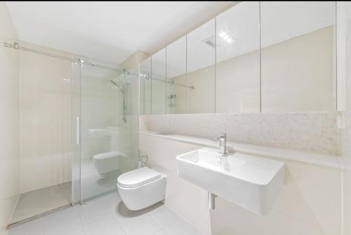 a white bathroom with a toilet and a sink at Stylish 1Bedroom Apartment with Study and Parking Near Sydney Airport in Sydney