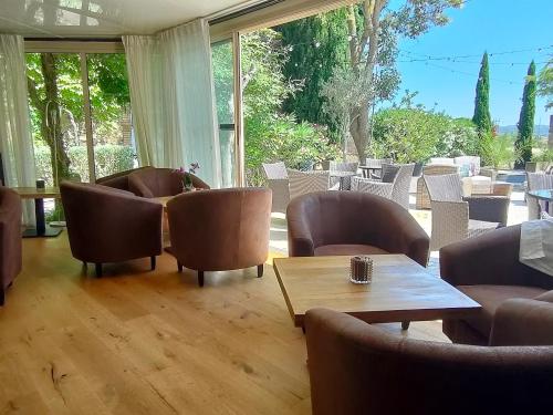 a living room with chairs and a table and windows at Hôtel Restaurant L'Art des Mets by Côté Jardin in Conilhac-Corbières