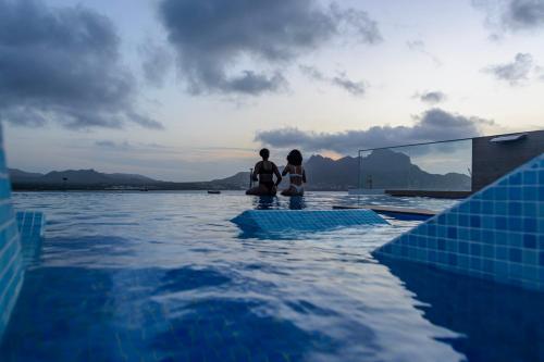 two people sitting on the edge of a swimming pool at Ouril Mindelo in Mindelo