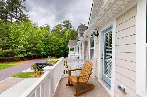 a porch with a wooden chair on a white house at The Peninsula --- 22308 Dune Cir 74 in Millsboro