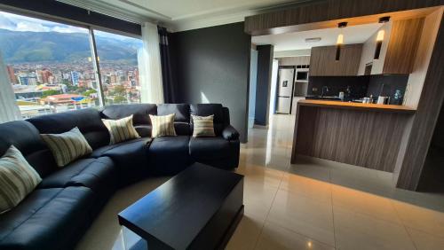 a living room with a black leather couch and a kitchen at Premium Apartamentos Torre Azul in Cochabamba