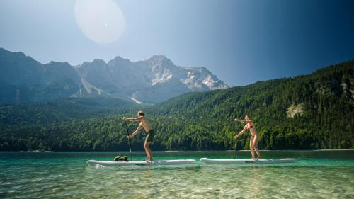 two people are standing on surfboards in the water at Eibsee Hotel in Grainau