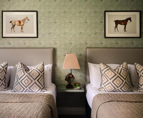 two beds in a hotel room with paintings of a horse on the wall at Horse & Jockey Hotel in Horse and Jockey
