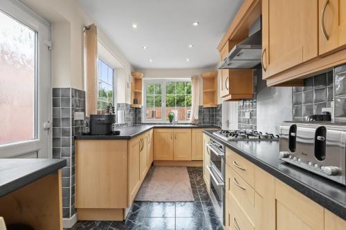a large kitchen with wooden cabinets and black counter tops at Modern 4-Bed Serviced Apartment- Free Parking Wi-Fi - Near CBS Arena -M6 -UHCW in Exhall