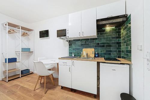 - une cuisine avec des placards blancs et un mur en carrelage vert dans l'établissement Cosy studio near Montparnasse, à Paris