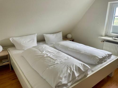 Una cama con sábanas blancas y almohadas. en Thora Jaiken Hüs Thora Jaiken, Apart Eike, en Rantum