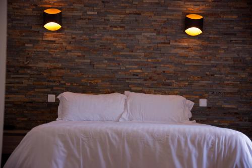 a white bed with two pillows and a brick wall at Auberge Val Moureze Hôtel & Spa in Mourèze