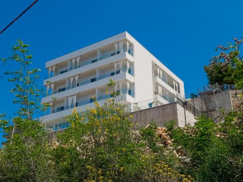 a white apartment building on a hill with trees at Sunset Shoreline Saranda - Sea View - Free Private Parking - Pool in Sarandë
