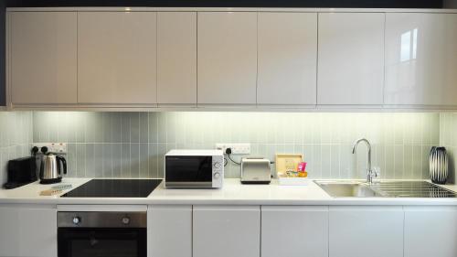 a kitchen with white cabinets and a sink and a microwave at Trident Court Apartments in Taunton