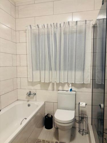 a white bathroom with a toilet and a bath tub at Self Catering 2 Bedroom Apartment in Matsapha