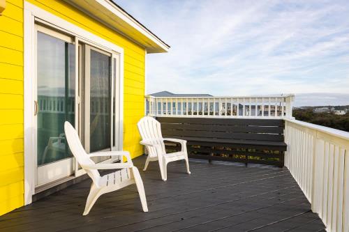 a yellow house with two chairs on a balcony at Semi Ocean Front Luxury Home Pool Spa Game Room in Duck