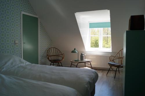a bedroom with a bed and two chairs and a window at Vakantiehuis 't Boerenhuis in Aagtekerke