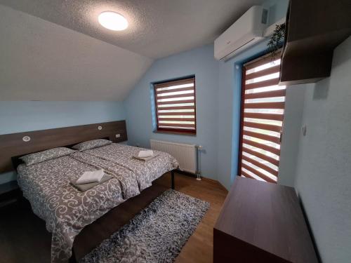 a bedroom with a bed and a table and two windows at Djuric Vacation House in Laktaši