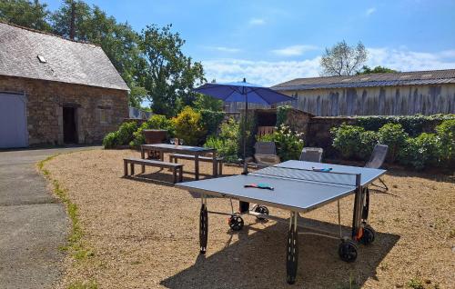 Dos mesas de ping pong y una sombrilla en un patio. en Ravissante Maison Bretonne, en Pleumeur-Gautier