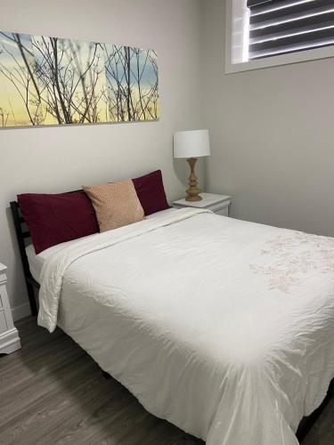 CalgaryThe Willow Nest lower suite的卧室里有一张床，上面铺着白色的床单和红色的枕头