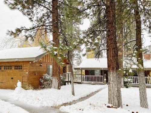 a house covered in snow in front of trees at Big Wood Pines - Relaxing home with a large fenced yard for your furry friends to enjoy! in Big Bear City