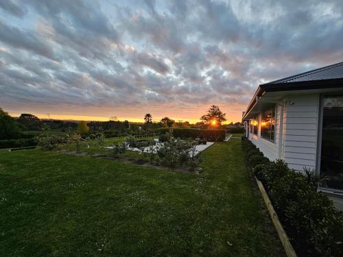 a house with a yard with a sunset in the background at Luxury B&B Steps Away From Most Wedding Venues of Kumeu! in Kumeu