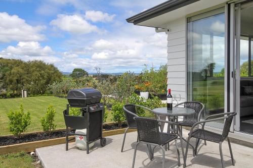 a grill on a patio with a table and chairs at Luxury B&B Steps Away From Most Wedding Venues of Kumeu! in Kumeu