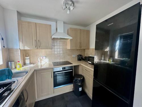a kitchen with wooden cabinets and a black refrigerator at Sianavi Apartments - Caspian Way, Purfleet in Purfleet