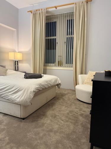 a bedroom with a bed and a chair and a window at Homely in Hampden in Glasgow