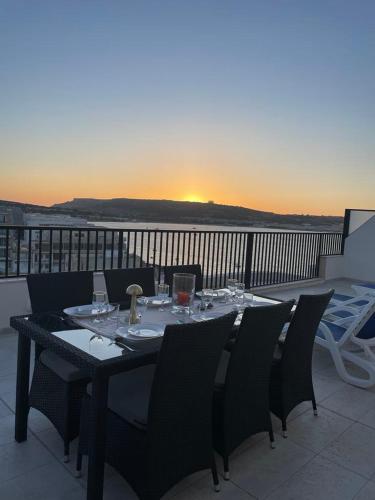 a table with wine glasses on a balcony with the sunset at Seafront Penthouse with Large Terrace and Panoramic Views-Mellieha Bay Ghadira in Mellieħa