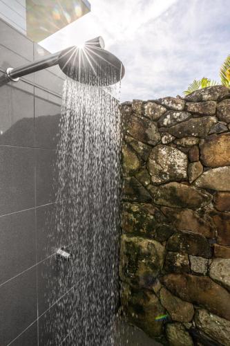 a shower in a bathroom with a stone wall at Byron Lux Beach Houses in Byron Bay