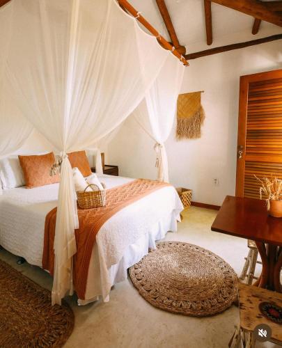 a bedroom with a bed with curtains and a table at Pousada Ó Paí, Ó in Caraíva