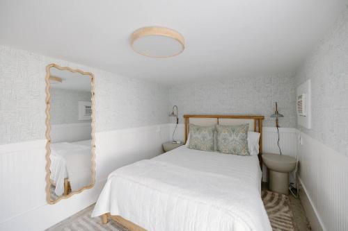 a white bedroom with a bed and a mirror at The Little Ray - 2 blocks to Beach - Backyard - Walk to Boardwalk in Carolina Beach