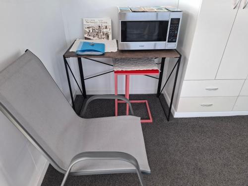 a desk with a microwave and a chair in a room at Private room with ensuite in Cable Bay
