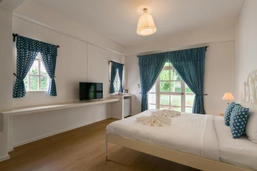 a bedroom with a bed with blue curtains and a tv at Villa La Flora Kaeng Krachan in Kaeng Krachan