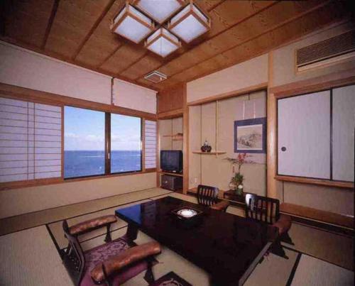 a living room with a table and chairs and windows at Futami Onsen Hotel Seikai in Ise