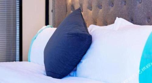 a blue pillow sitting on a bed with white pillows at Xana Hotelle Chengdou Xindu Sanhechang Metro Station in Chengdu