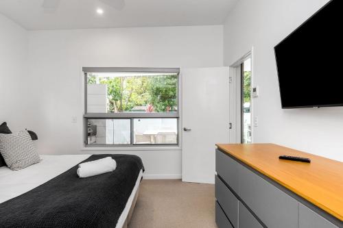 a bedroom with a bed and a flat screen tv at Fat Frog Beach Houses in Byron Bay