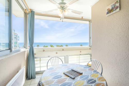 une table et des chaises dans une pièce avec une grande fenêtre dans l'établissement Canet plage face à la mer, à Canet