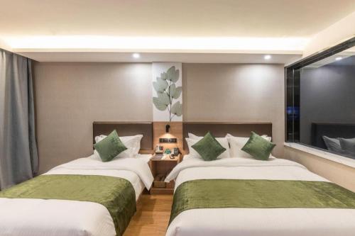 two beds in a hotel room with green pillows at GreenTree Inn Express Zhangjiagang Hexing Town Shazhou Professional Institue of Technology in Qiwei