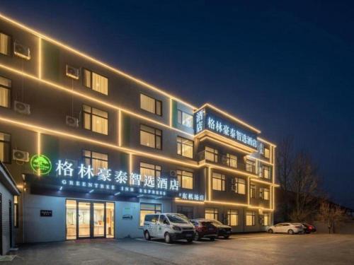 a building with cars parked in a parking lot at night at GreenTree Inn Express Qingdao Jiaodong International Airport in Qingdao