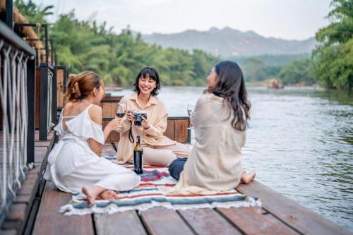 three women sitting on a dock with a bottle of wine at The River Life Resort in Ban Kaeng Raboet
