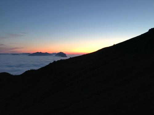 a silhouette of a mountain with the sun setting over the clouds at Ferienwohnungen Schantl in Schoppernau