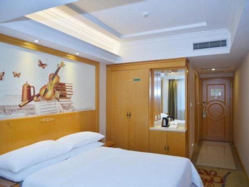a bedroom with a white bed and a painting of a guitar at Vienna Hotel Shenzhen Bao'an Airport Taoyuanju Pingluanshan Metro Station in Shenzhen