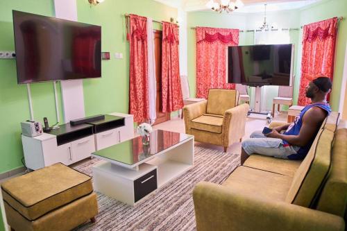a man sitting in a living room with a flat screen tv at Appartements et studios meublés kahak in Douala