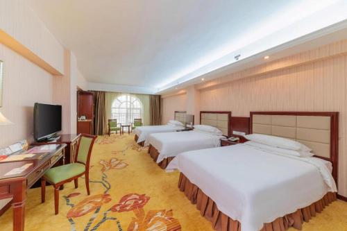 a hotel room with three beds and a desk and a television at Vienna Hotel Meizhou Mei County Airport in Meizhou