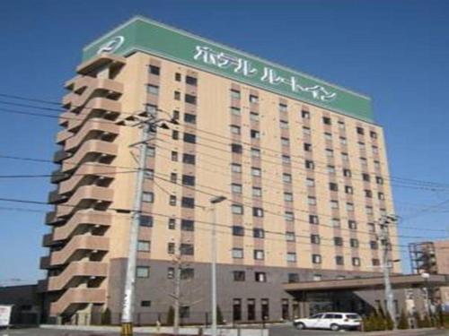 a large building with a green and white sign on it at Hotel Route Inn Furukawa Ekimae in Osaki
