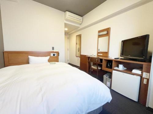 a hotel room with a white bed and a tv at Hotel Route Inn Furukawa Ekimae in Osaki